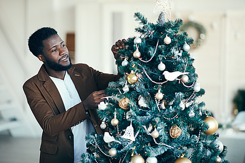 Waist up portrait of smiling African-American man decorating Christmas tree at home, copy space