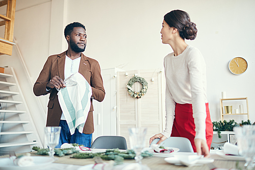 Portrait of modern young couple looking at each other while preparing for Christmas dinner party, copy space