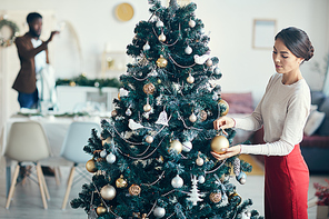 High angle portrait of modern couple preparing for dinner party at home, focus on young woman decorating Christmas tree in foreground, copy space