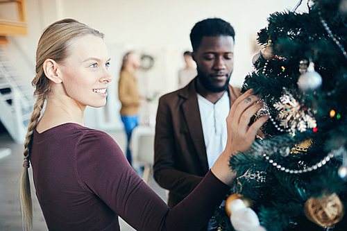 Waist up portrait of beautiful young woman looking at decorations on Christmas tree during party banquet, copy space