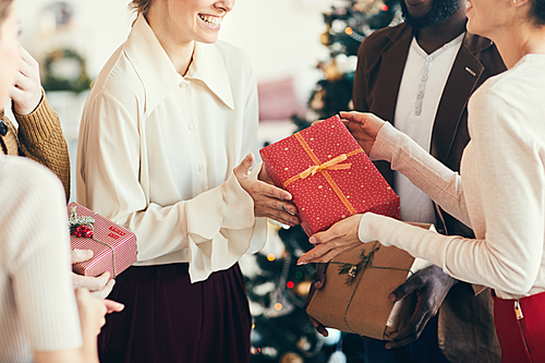 Cropped portrait of elegant young people exchanging gifts during Christmas party, focus on red box with golden ribbon, copy space