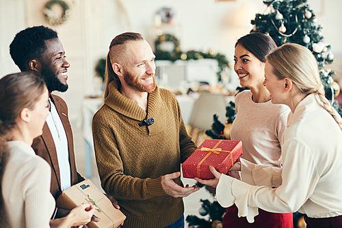 Multi-ethnic group of cheerful young people exchanging gifts during Christmas party, copy space