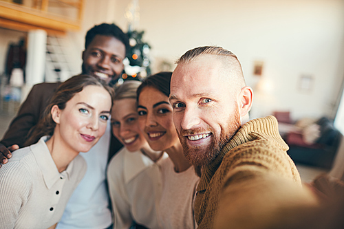Multi-ethnic group of contemporary adult people smiling at camera while taking selfie photo during Christmas party