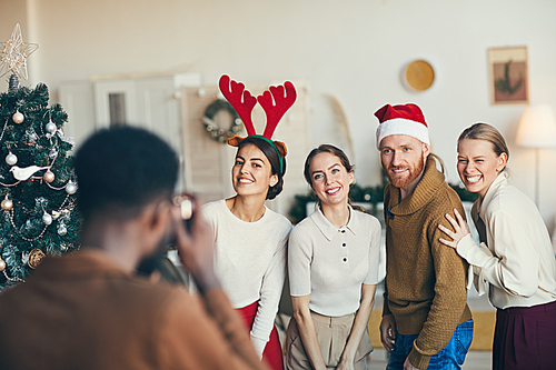 Group of contemporary adult people posing for photograph during Christmas party, wearing Santa hats and costumes, copy space