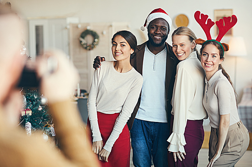 Multi-ethnic group of friends posing for photograph during Christmas party, all wearing Santa hats and costumes, copy space