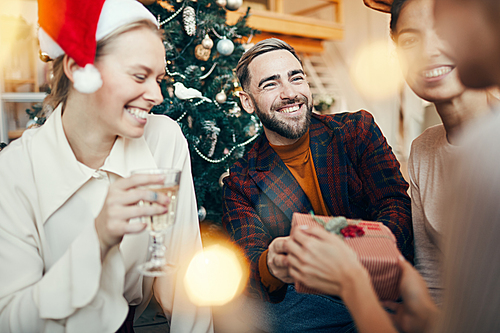 Portrait of elegant adult man smiling happily while exchanging gifts with friends during Christmas party
