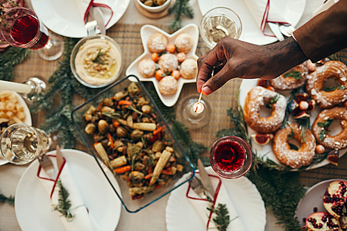 Top view background of hand lighting candle over rustic Christmas table with delicious homemade food decorated with fir branches, copy space