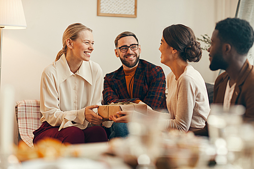 Group of elegant adult people exchanging presents on Christmas, focus on beautiful blonde woman smiling happily holding gift box