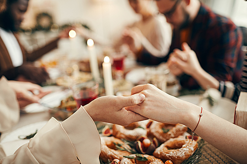 Close up of people sitting at dining table on Christmas and joining hands in prayer, copy space