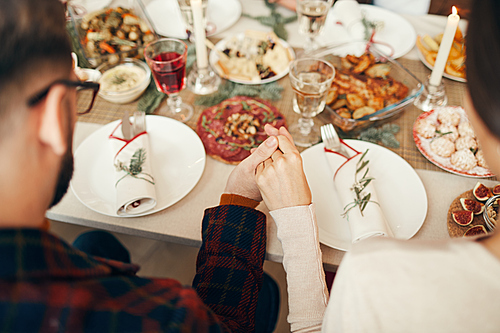 Above view close up of people sitting at dining table on Christmas and joining hands in prayer, copy space