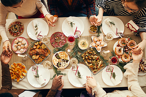 Above view at group of people sitting at dining table on Christmas and joining hands in prayer, copy space