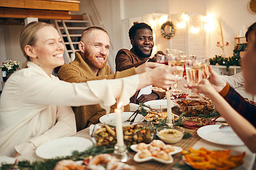 Multi-ethnic group of people raising glasses while celebrating Christmas with friends and family sitting at beautiful dinner table
