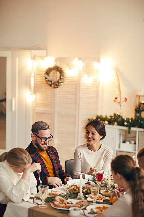 High angle view at successful adult couple laughing cheerfully while celebrating Christmas with friends at dinner table, copy space