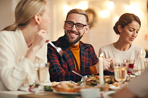 Portrait of handsome adult man smiling cheerfully while celebrating Christmas with friends and family at dinner table