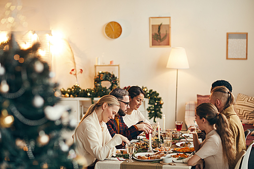 Wide angle view at modern young people celebrating Christmas sitting at dinner table in elegant dining room, copy space