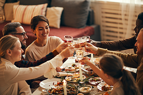 High angle view at elegant young people clinking champagne glasses while enjoying Christmas dinner at home, copy space