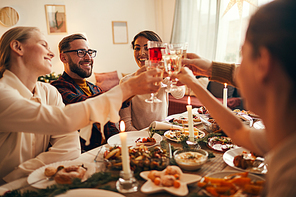 Side view portrait of elegant young people clinking champagne glasses while enjoying Christmas dinner at home