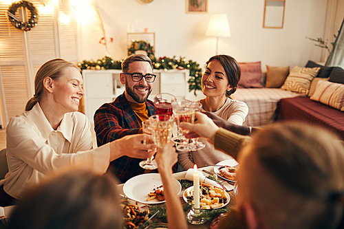 High angle portrait of cheerful adult people clinking champagne glasses while enjoying Christmas dinner at home, copy space