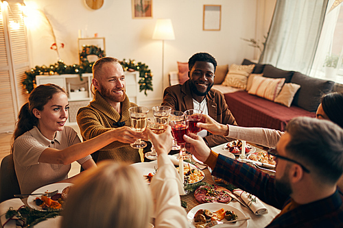 Multi-ethnic group of young people clinking champagne glasses while enjoying Christmas dinner at home, copy space