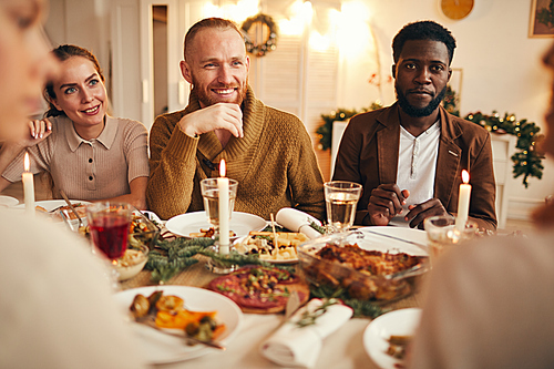 Poirtrait of multi-ethnic group of people enjoying dinner sitting at table with delicious food, focus on smiling bearded man in center