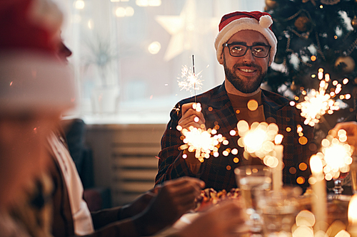 Portrait of cheerful bearded man wearing santa hat while enjoying Christmas celebration dining with friends and family