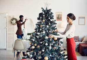 Side view portrait of elegant young woman decorating Christmas tree while preparing for dinner party with husband, copy space