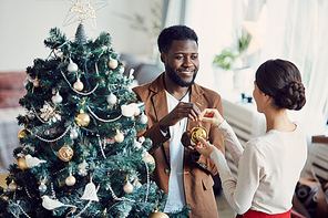 High angle portrait of smiling married couple decorating Christmas tree together standing in elegant living room, copy space