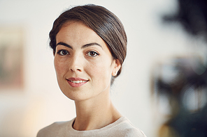 Head and shoulders portrait of elegant adult woman smiling at camera while posing in beautiful home, copy space