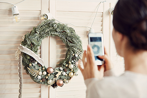 Back view portrait of young woman taking smartphone photo of beautiful Christmas wreath, copy space