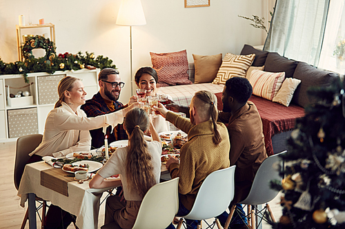 High angle view at group of elegant young people clinking glasses while celebrating Christmas at festive dining table, copy space