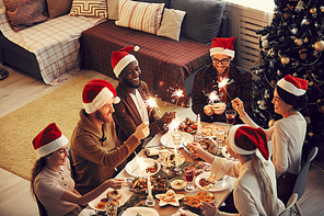 High angle view at group of young people holding sparkling lights while celebrating Christmas at festive dining table, copy space