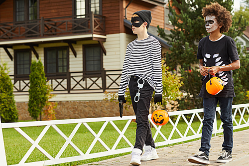 Full length portrait of two teenage boys wearing Halloween costumes walking outdoors in street while trick or treating with pumpkin baskets , copy space