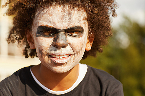 Head and shoulders portrait of tough African-American boy wearing skeleton costume posing outdoors on Halloween, lit by sunlight