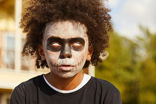 Head and shoulders portrait of African-American buy wearing scary skeleton costume posing outdoors on Halloween lit by sunlight, copy space