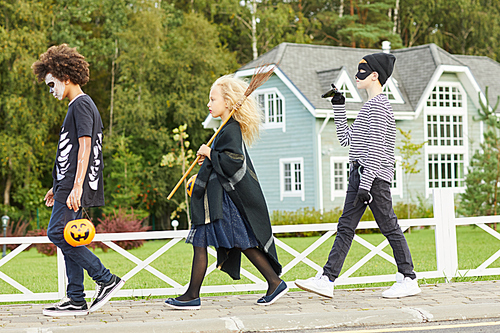 Full length side view at group of three children wearing Halloween costumes walking in row while trick or treating together