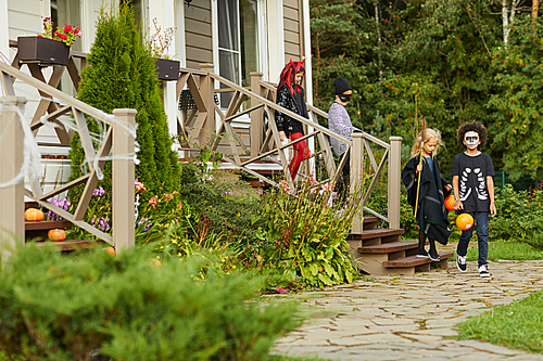 Full length portrait of group of children trick or treating on Halloween leaving house, copy space