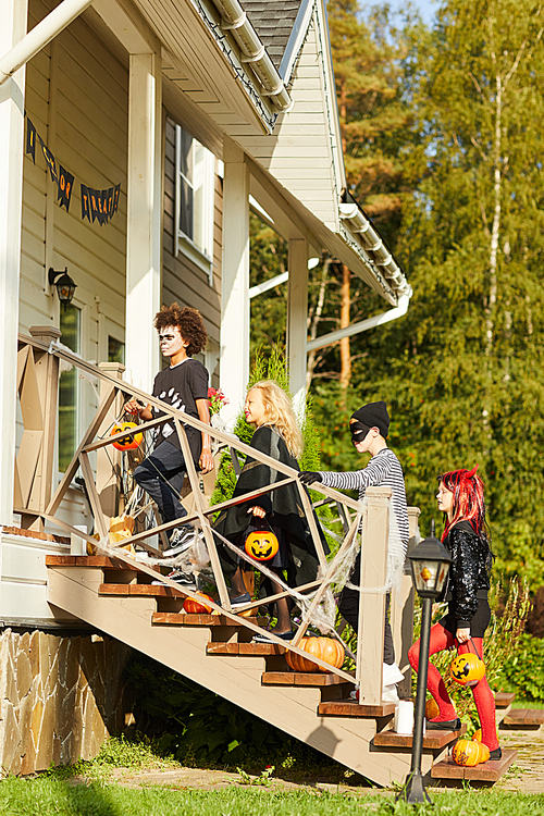 Full length side view portrait of group of children trick or treating on Halloween standing on stairs in row, copy space