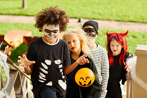 Portrait of multi-ethnic group of children trick or treating on Halloween standing on stairs in row, copy space