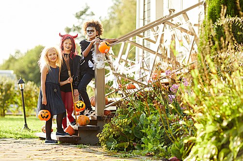 Full length portrait of multi-ethnic group of children trick or treating on Halloween, all smiling at camera while standing on stairs of decorated house
