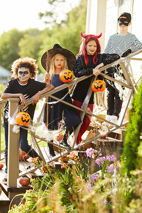 Multi-ethnic group of children wearing Halloween costumes standing on stairs of decorated house while enjoying trick or treating together