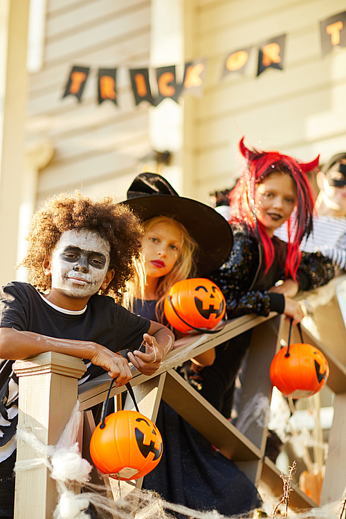 Multi-ethnic group of children wearing Halloween costumes  while standing on stairs of decorated house in trick or treat season