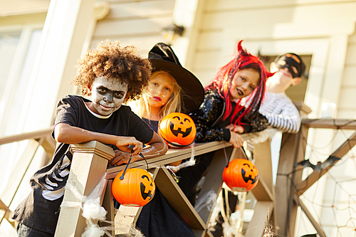 Multi-ethnic group of children wearing Halloween costumes smiling at camera while standing on stairs of decorated house in trick or treat season