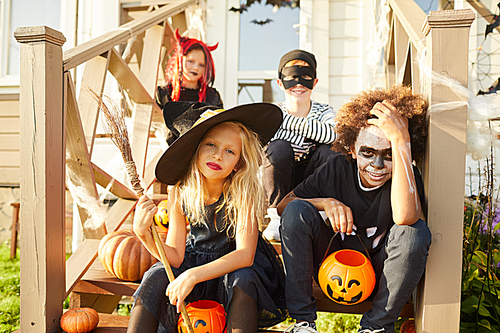 Multi-ethnic group of children wearing Halloween costumes  while sitting on stairs of decorated house in trick or treat season