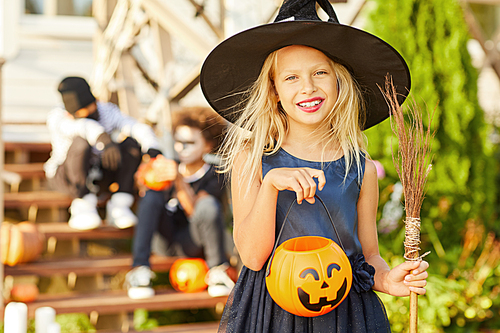 Waist up portrait of cute little girl wearing Halloween costume  while posing outdoors holding pumpkin basket, copy space