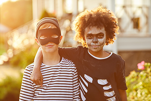 Waist up portrait of two boys wearing Halloween costumes posing outdoors lit by sunlight, copy space