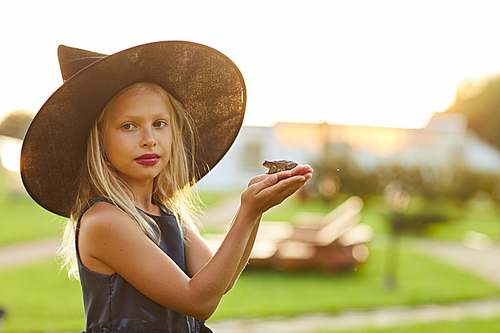 Waist up portrait of cute little witch holding frog while posing outdoors on Halloween, copy space