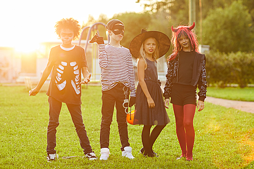 Multi-ethnic group of kids wearing Halloween costumes  while posing outdoors lit by sunlight, copy space