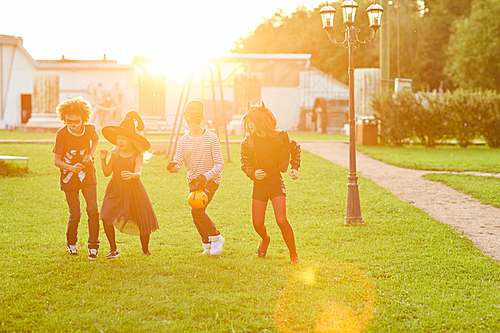 Multi-ethnic group of kids wearing Halloween costume shaving fun running outdoors lit by sunlight, copy space