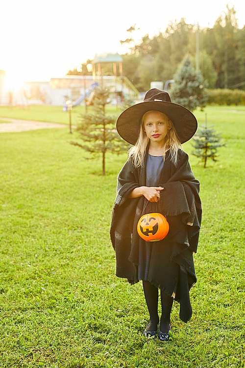 Full length portrait of cute teenage girl dressed as witch posing outdoors on Halloween and holding trick or treat basket, copy space