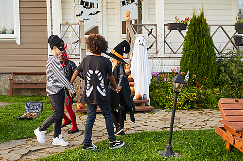 Multi-ethnic group of children playing Halloween games outdoors by decorated house, copy space